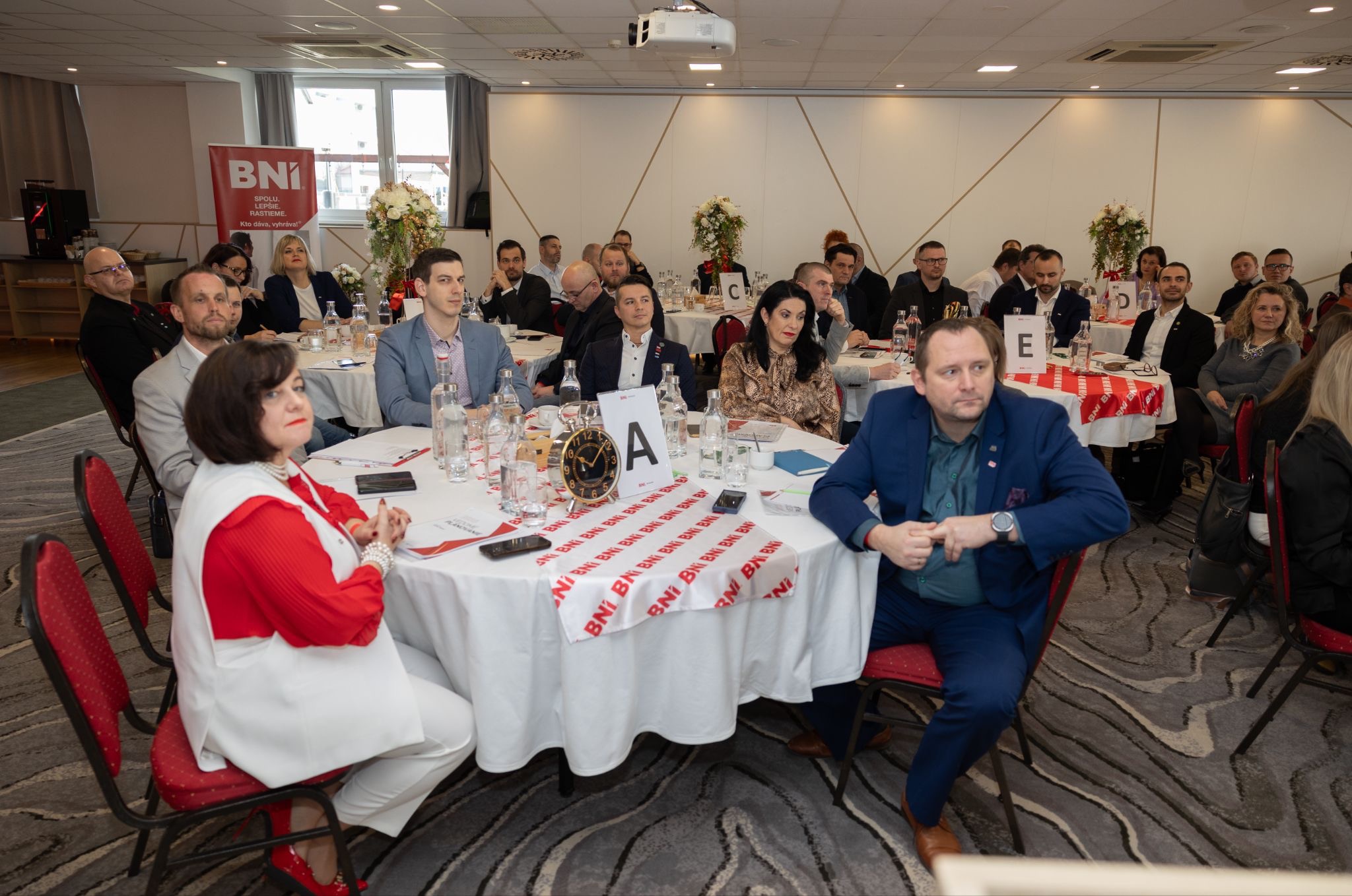 BNI networkingové podujatie s podnikateľmi sediacimi pri stoloch počas spoločného stretnutia.